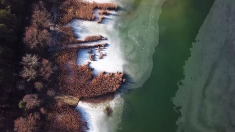 Aerial-landscape-descending-tilting-shot-of-barely-frozen-lake-with-reeds-and-hill,-Hungary,-Europe