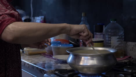 ethnic minority woman stirring food in steel pot on cooker