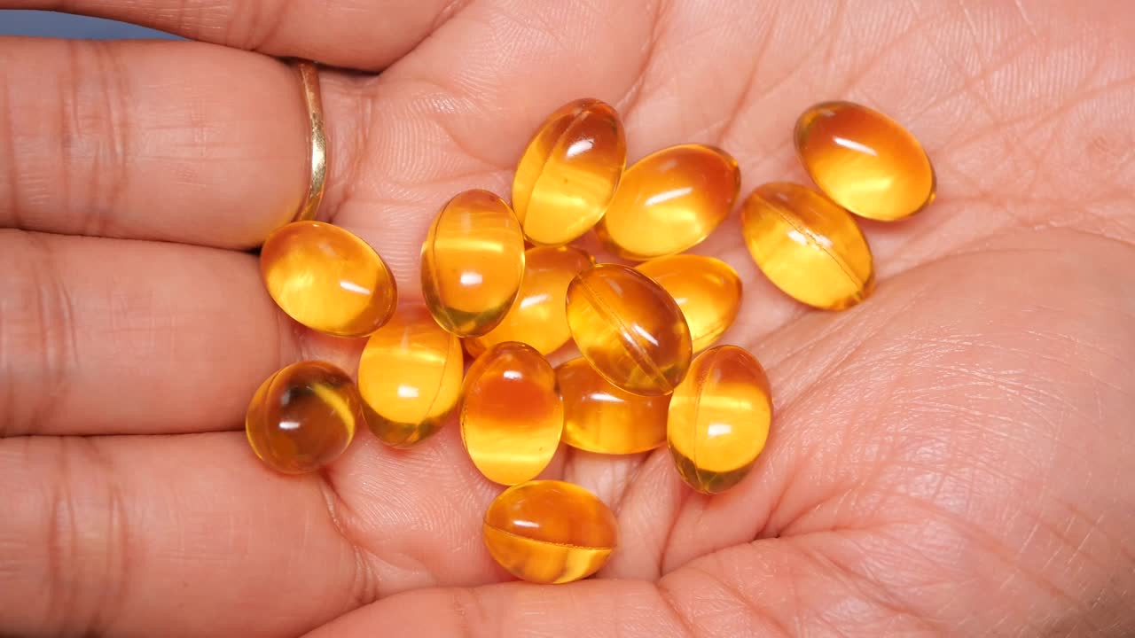 Primo piano di una mano che tiene capsule vitaminiche gialle