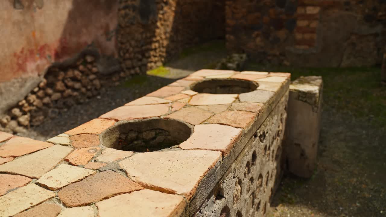 Bancone in pietra di Pompei illuminato dal sole con aperture rotonde per vasi, che mostra l'architettura conservata di un servizio di ristorazione romano in un'antica bottega o ambiente di cucina