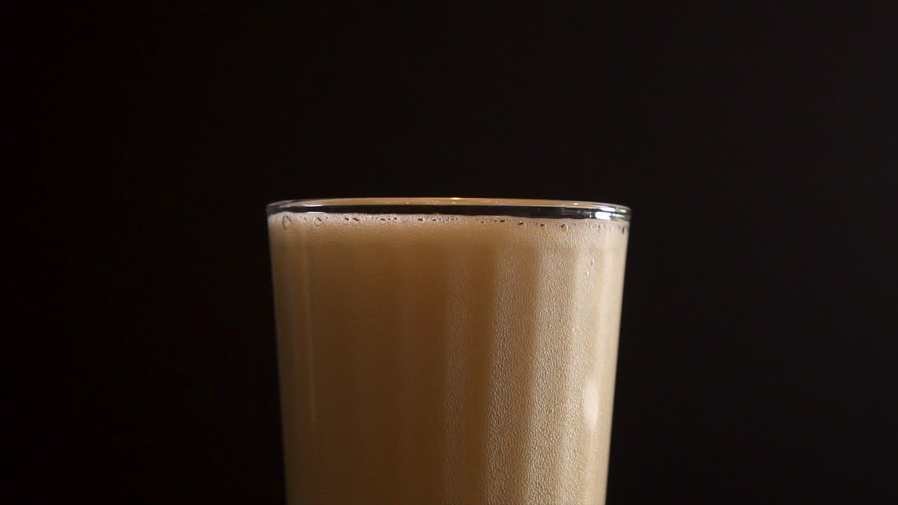 Beer foam bubbling into a transparent glass, close up slow motion
