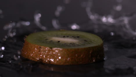 una rebanada de kiwi cayendo sobre un fondo negro húmedo