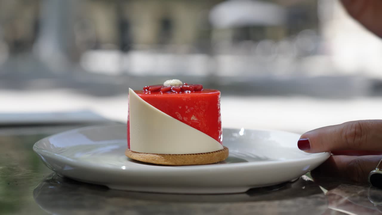 close-up of a white plate with a gourmet dessert in the centre, a woman's hand with red nail polish reaching out to take a spoonful