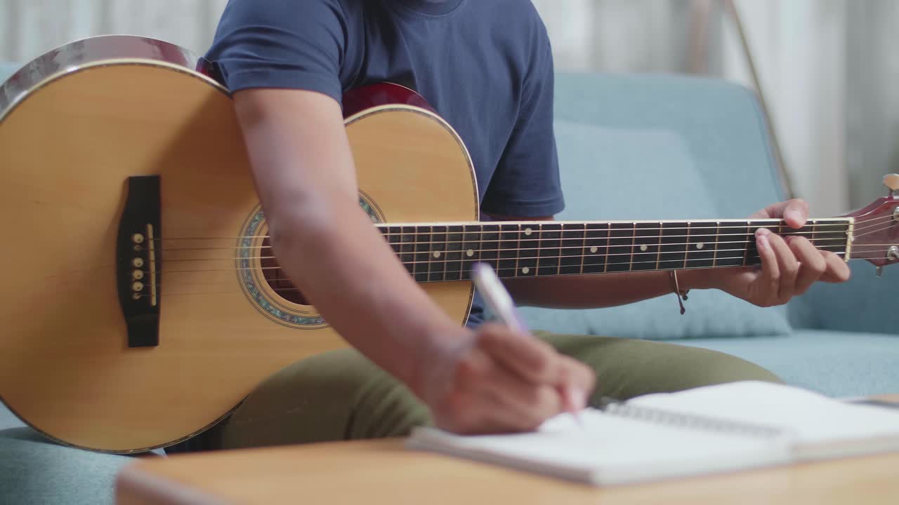 primer plano de un compositor asiático con una guitarra celebrando por terminar de componer música en papel en casa