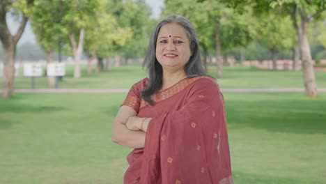 portrait of happy indian old woman standing crossed hands in park