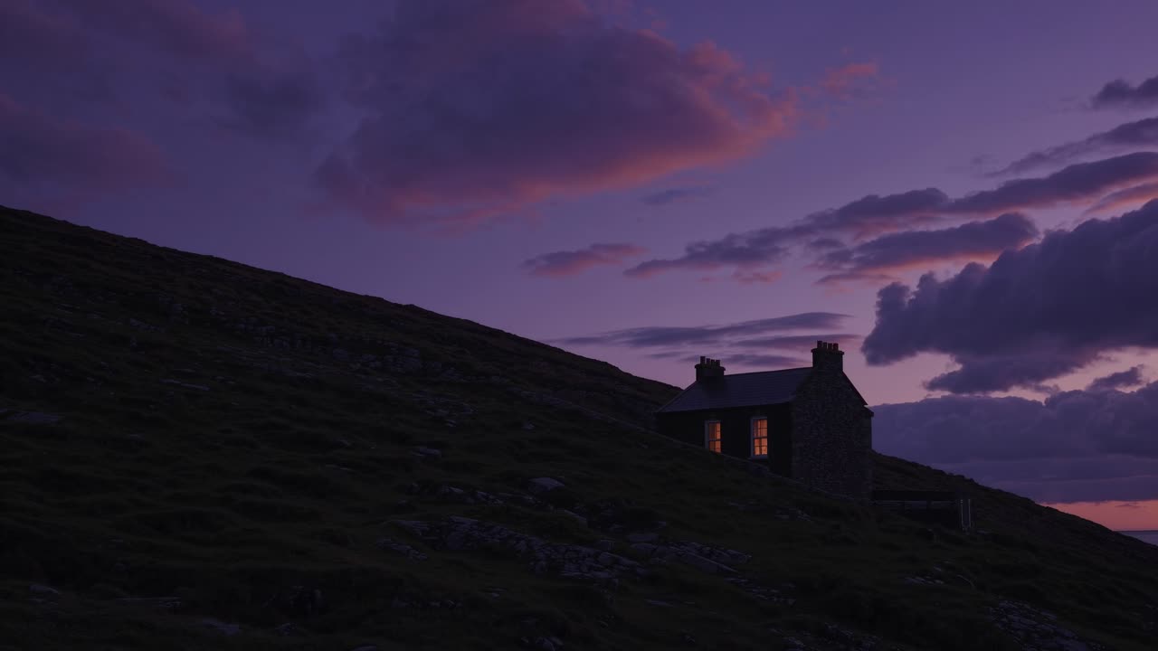 Warm lights glowing from windows of a solitary house nestled on a hillside, creating a cozy scene against a backdrop of dramatic sunset hues and a cloudy sky