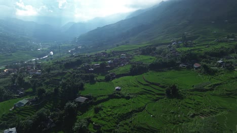drone zooms in above rice fields and rural homes surrounded by vegetation in sa pa's mountainous landscape.