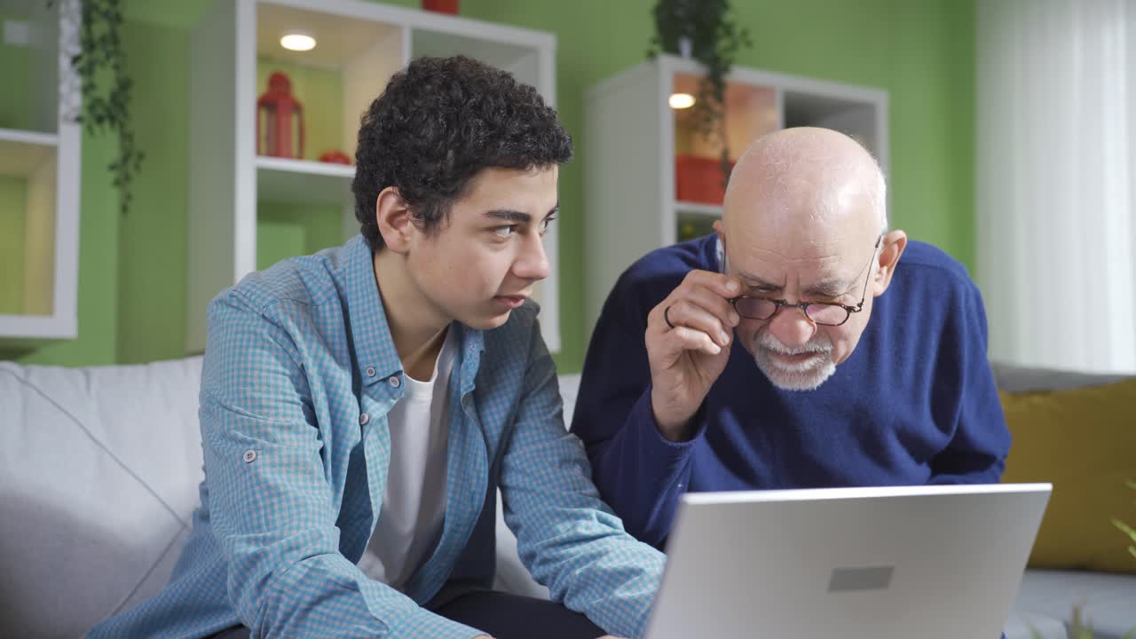 Curious grandfather looking at what his cute grandson is doing while looking at laptop.