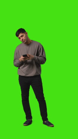 video vertical de larga duración de un hombre mirando un mensaje de texto en un teléfono móvil de pie contra la pantalla verde 5