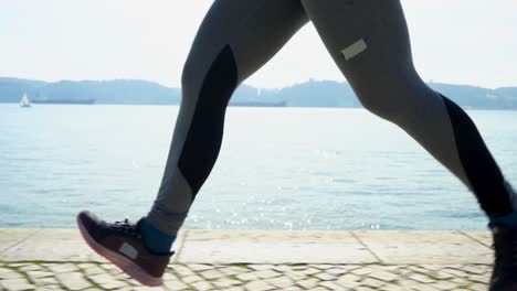 Legs-of-sporty-young-woman-running-near-river