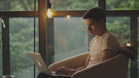 caucasian man sits on the couch and types on laptop keyboard