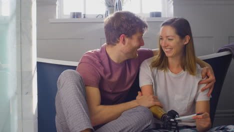 Excited-Couple-With-Woman-With-Prosthetic-Arm-Sitting-On-Bathroom-Floor-With-Positive-Pregnancy-Test