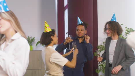 grupo de colegas multiétnicos sosteniendo una copa de champán, bailando y divirtiéndose juntos en la fiesta de la oficina
