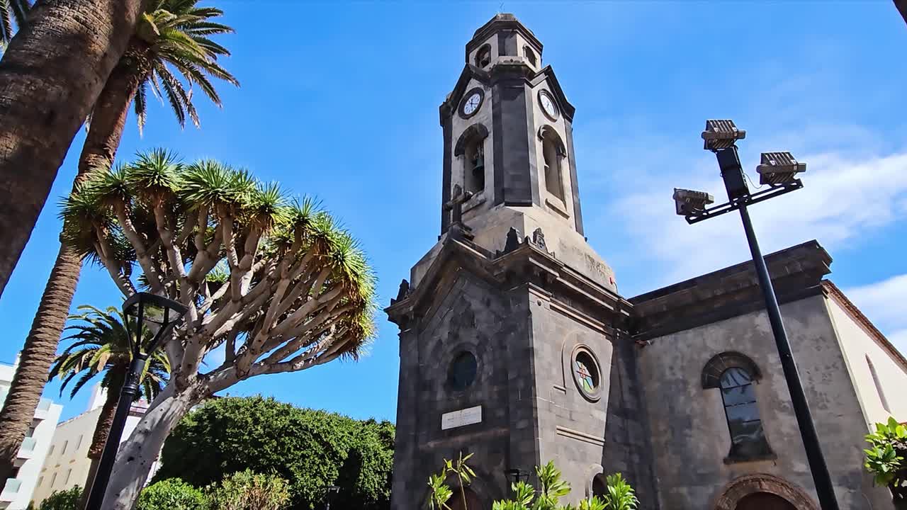 A historic clock tower in Puerto, Spain, surrounded by palm trees and blue skies
