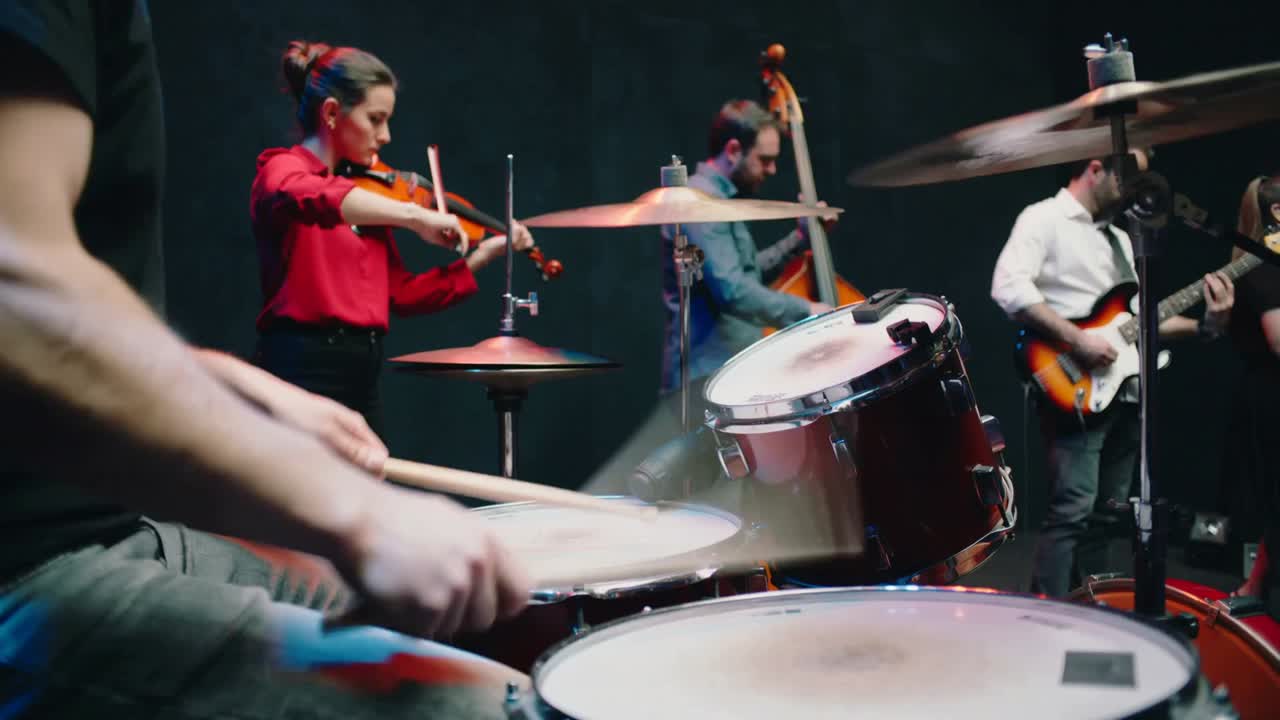 Batterista esordiente con maglietta scura che suona la batteria sul palco, ritmo incalzante con violino e basso