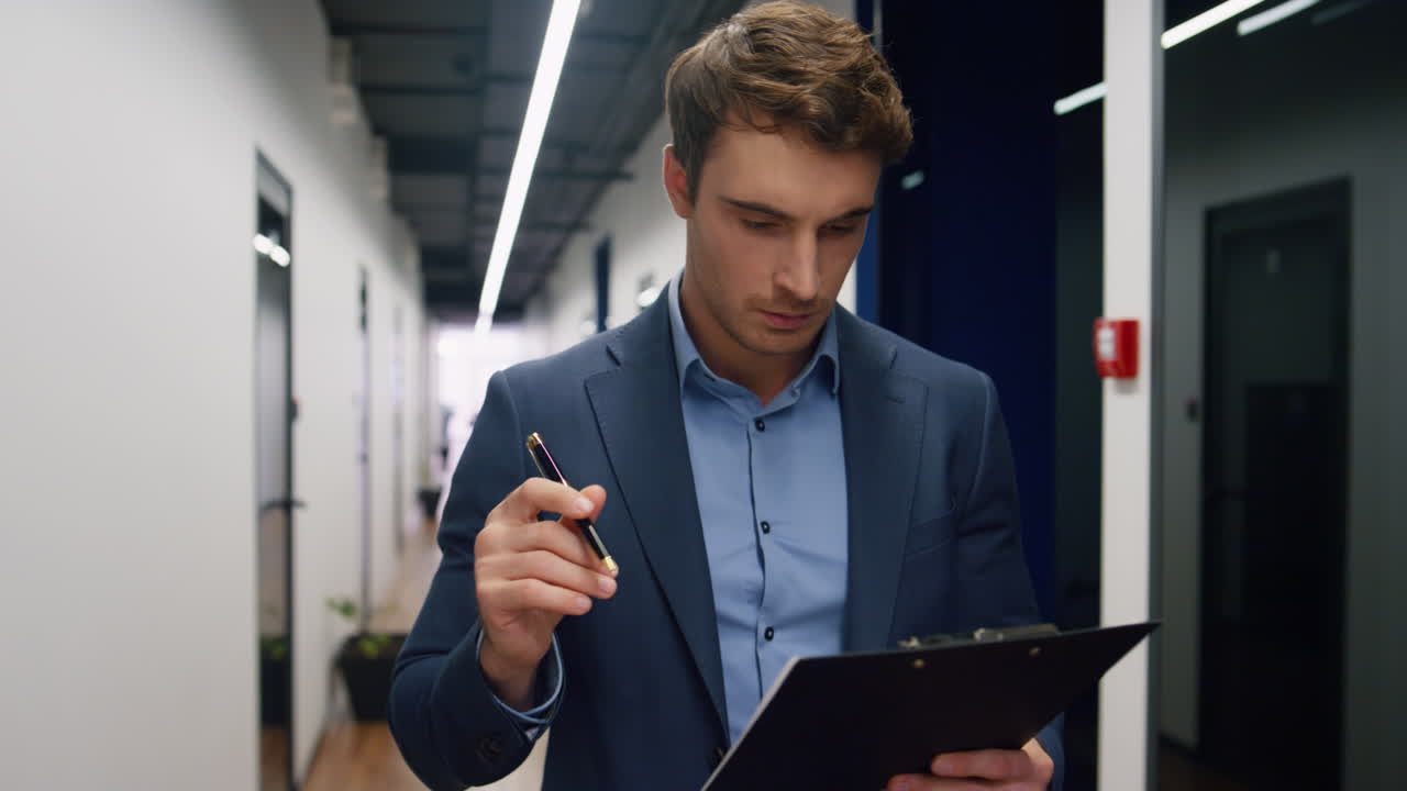 Focused manager looking documents on clipboard. Company ceo walking hallway