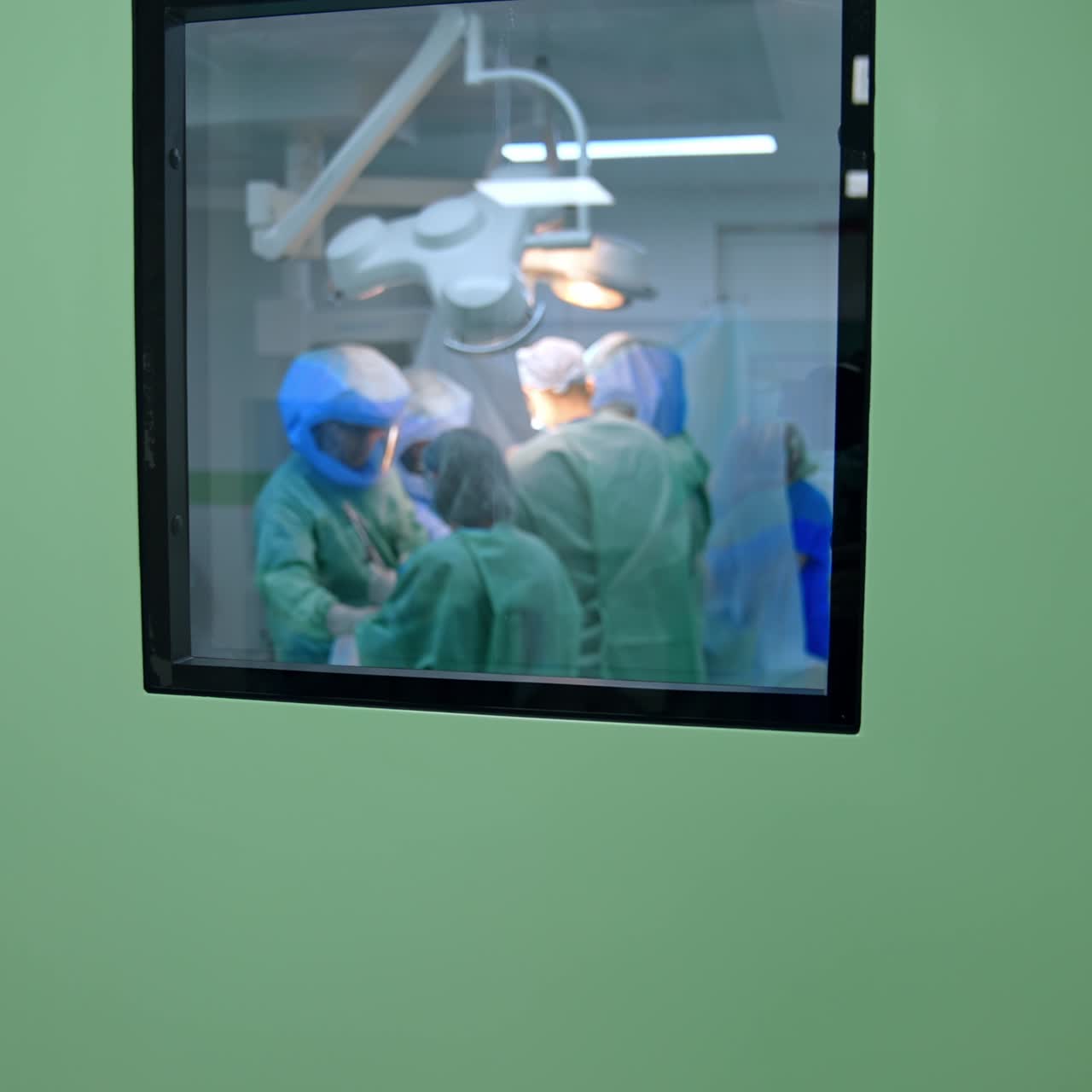 Puerta ligeramente abierta a un quirófano moderno. Una vista a través de la ventana de la puerta hacia los médicos trabajando dentro