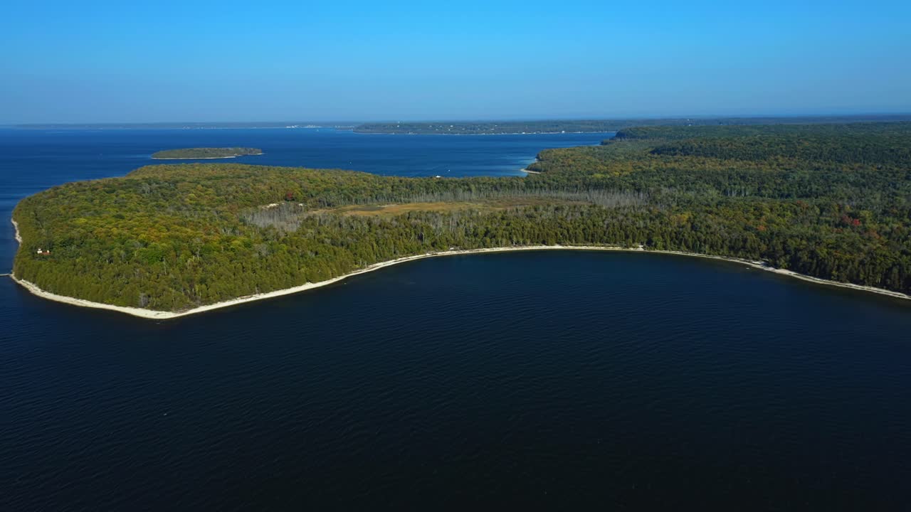 The smooth curve of Door County’s forested shoreline arcs into the bay, where dark blue waters glisten beneath clear skies, tracing the quiet meeting of land and lake
