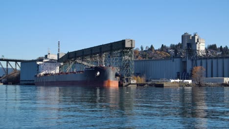 cargo ship docked at industrial port with grain elevator under clear blue sky in vancouver, canada