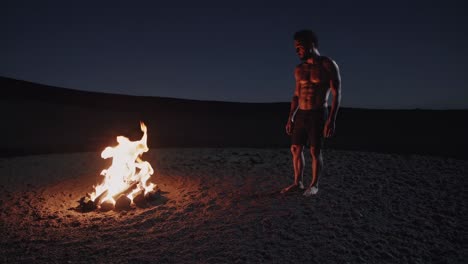 shirtless athlete warming up near a bonfire in the desert at night, illuminated by the warm glow of the flames, creating a dramatic and evocative scene of strength and resilience