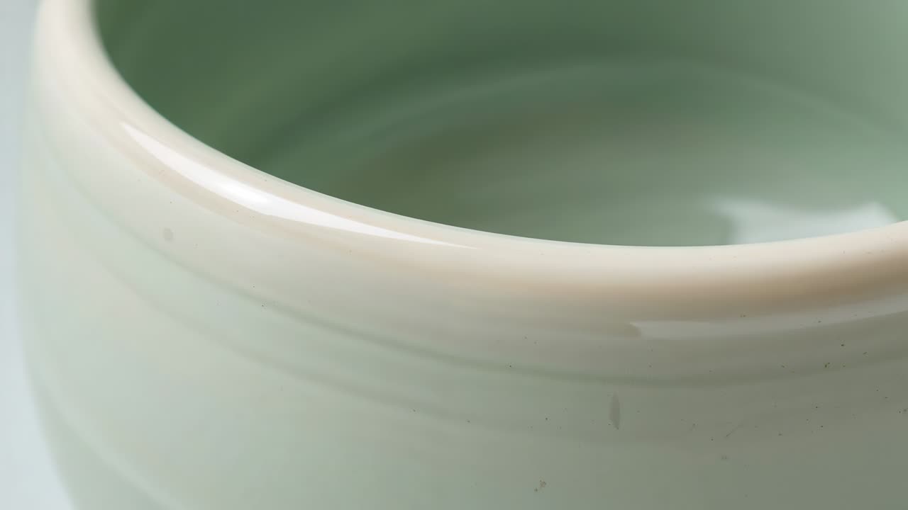 Telecamera in studio con movimento orizzontale che rivela interni lucidi, mostrando bordo bianco e smalto celadon sul vaso