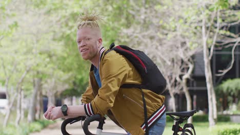 Portrait-of-smiling-albino-african-american-man-with-dreadlocks-in-park-with-bike-looking-at-camera