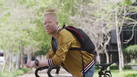 retrato de un hombre afroamericano albino sonriente con rastas en el parque con una bicicleta mirando a la cámara
