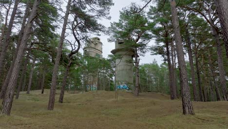 Establishing-aerial-view-of-old-Soviet-military-concrete-observation-watchtower,-pine-tree-forest,-Liepaja-,-military-heritage,-Nordic-woodland,-low-wide-drone-shot-moving-forward