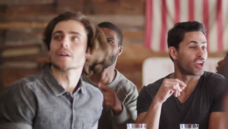 group of male friends celebrating whilst watching game on screen in sports bar