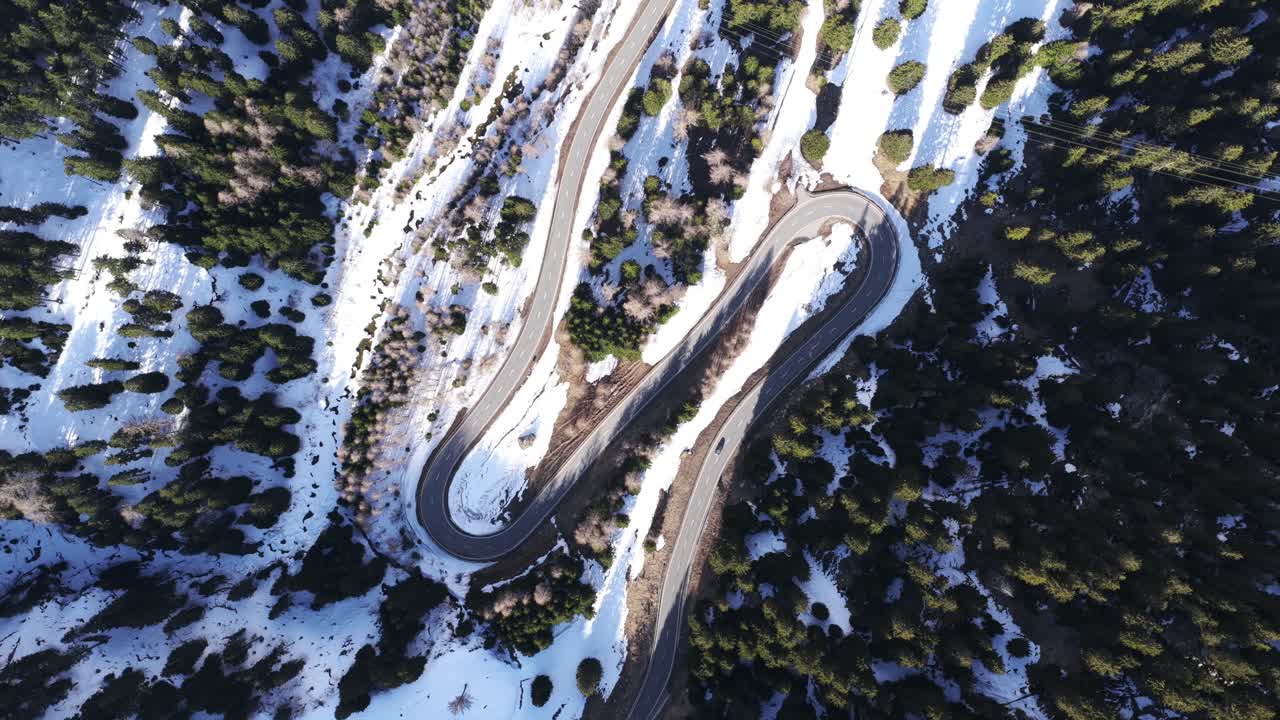 Top-down aerial rotates slowly above snowy switchback road in Maloja Pass, Switzerland