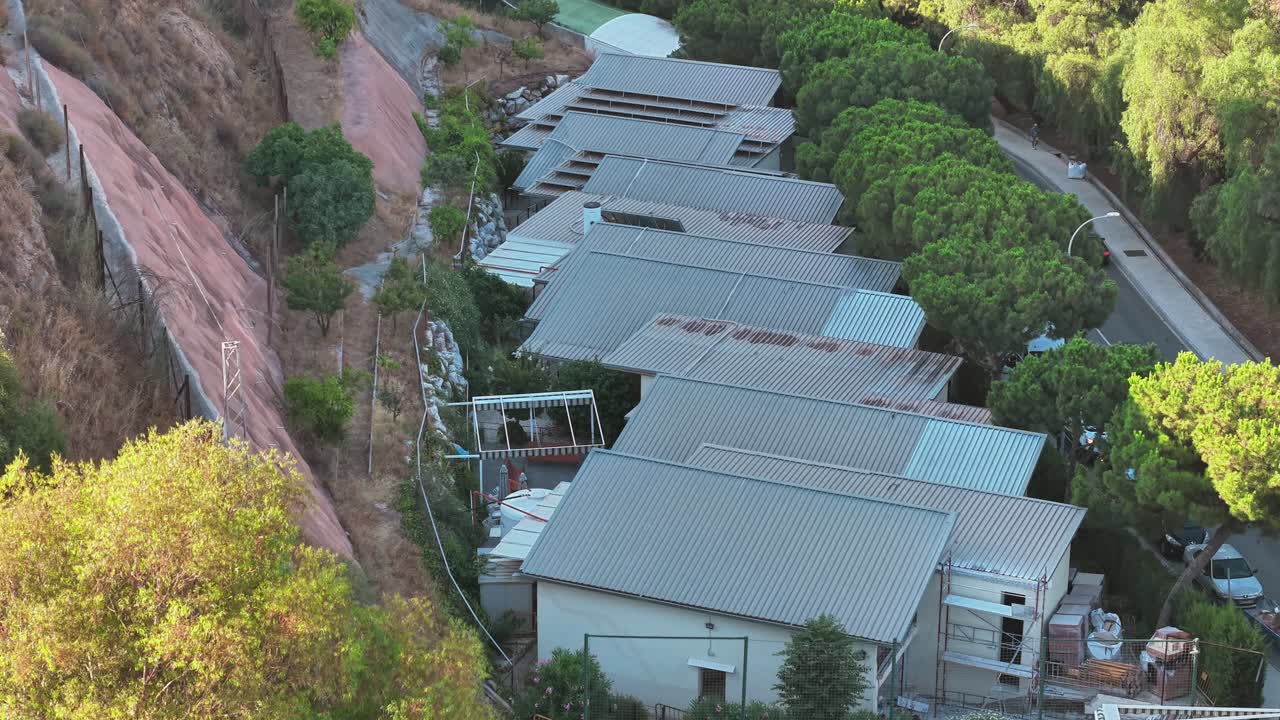 An aerial drone shot captures a residential area in Vicente Paul, Spain, featuring modern homes, lush greenery, and a blue sports court. Highlights urban living and recreational spaces