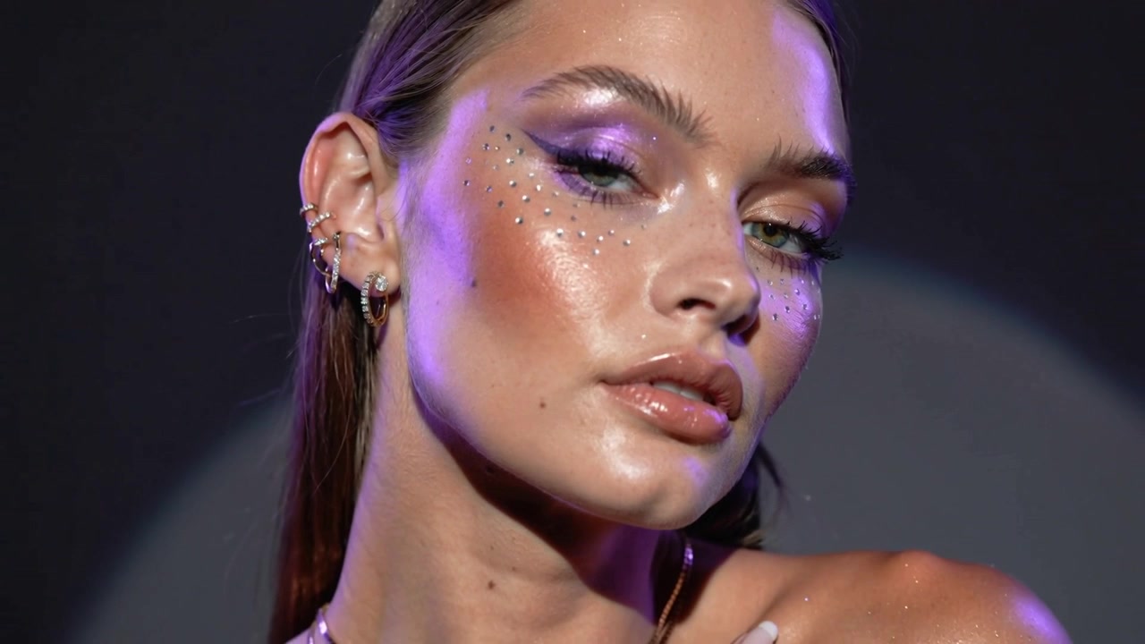 Telecamera in funzione, modella con strass che gira la testa e si tocca la clavicola in studio per una pubblicità di bellezza.