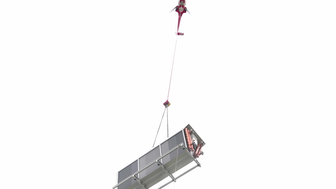 Helicóptero industrial realiza transporte aéreo de carga pesada de una unidad de refrigeración HVAC para su colocación de precisión en la azotea de un rascacielos en construcción.