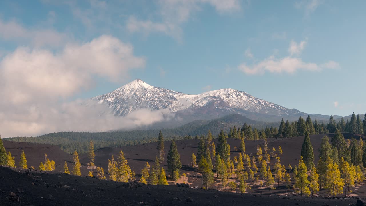 Timelapse across black volcanic sand with views of snow-covered Mount Teide in the background. Clouds roll over the landscape creating dynamic atmospheric movement in Teide National