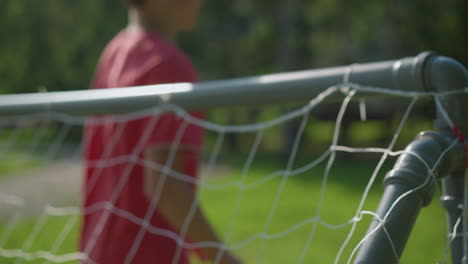 a blurred view of a goalkeeper in red attempts to save a ball shot into the net in a grassy field