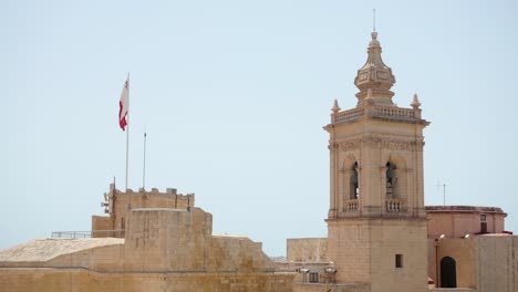 partial view of cathedral of the assumption from the walls of the citadella of victoria in gozo with maltese flag