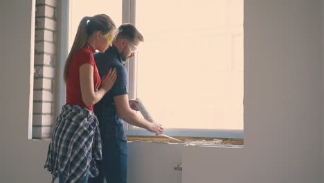 man in goggles with wife apply spray foam insulation on sill