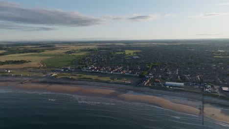 drone clip showing small english coastal town next to sandy beach with gentle waves lapping on the shoreline