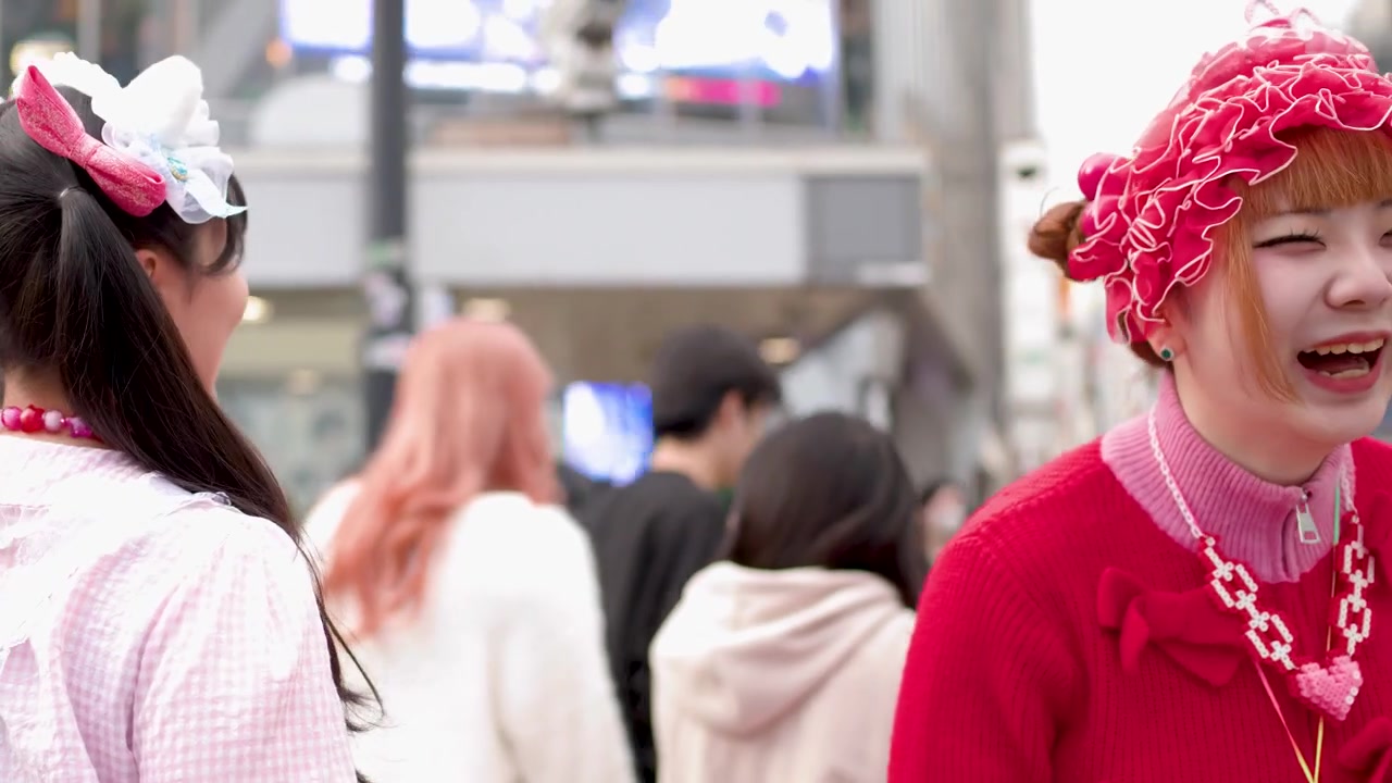 Dua wanita muda dengan pakaian decora warna-warni menari dan tertawa di jalanan Tokyo yang ramai
