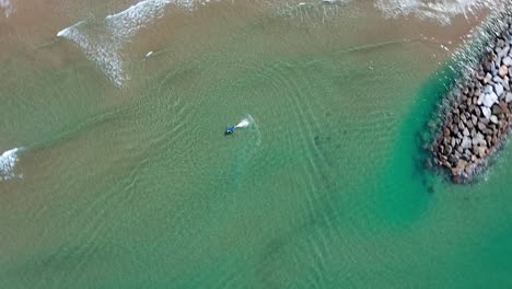 Skate-surfer-in-clear-waters-near-port-ginesta,-barcelona,-with-waves-lapping-the-shore,-aerial-view