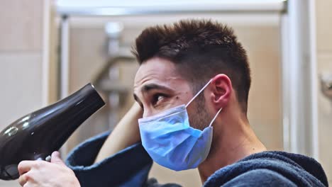 el hombre se seca el pelo en el baño con una máscara médica protectora