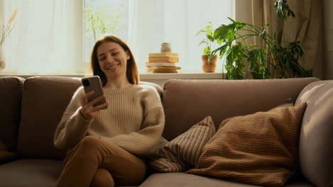 woman happily using smartphone on couch at home