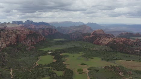 high and wide slow panoramic drone shot of zion nation park valley, green grass and prominent red rocks