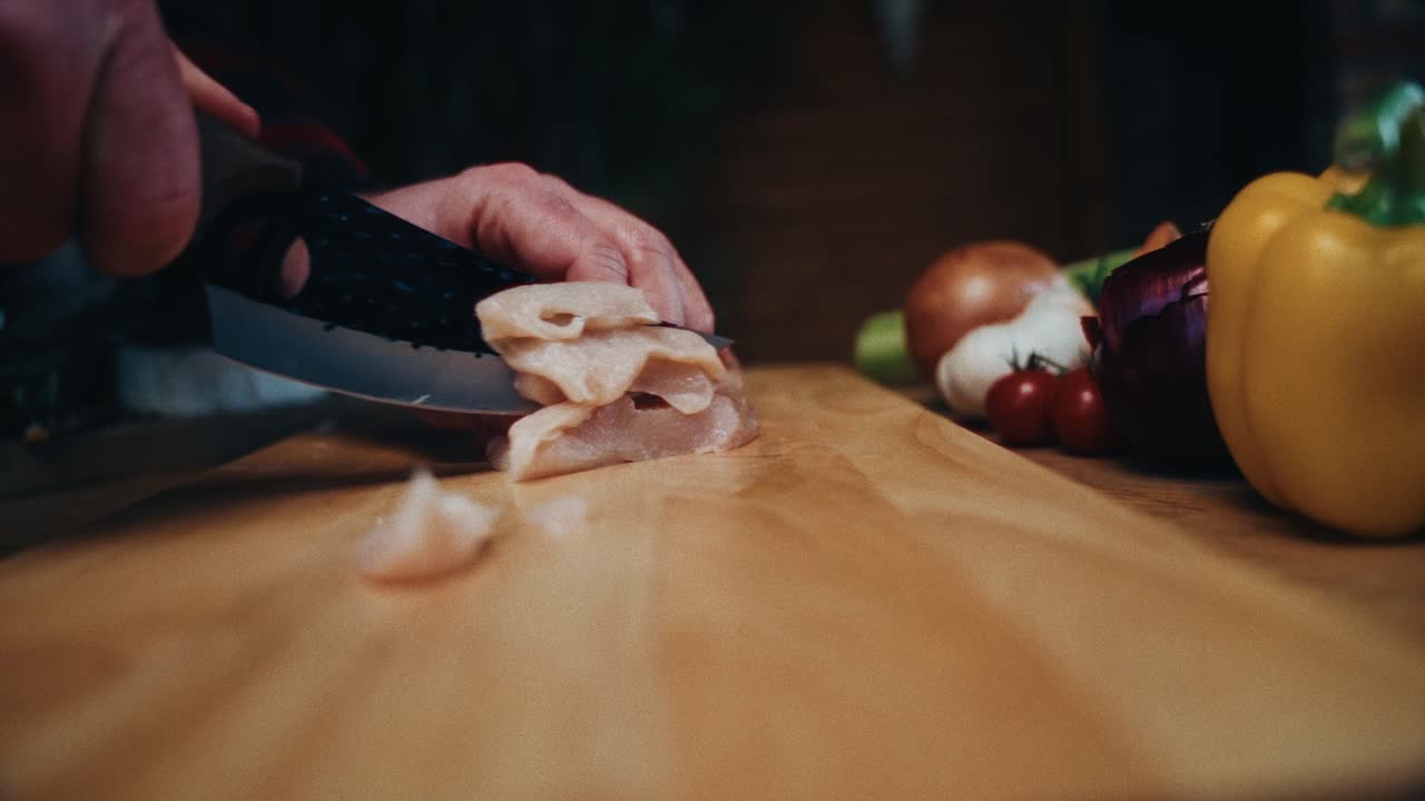 pollo fresco siendo cortado en una tabla de corte de madera con verduras en el fondo