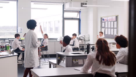 female high school tutor teaching students in uniforms sitting at work benches in science class