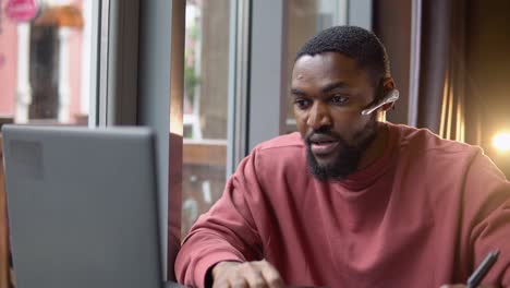 african american young man wear headset communicating by conference call speak looking at computer in cafe. video chat job interview or distance language course class concept