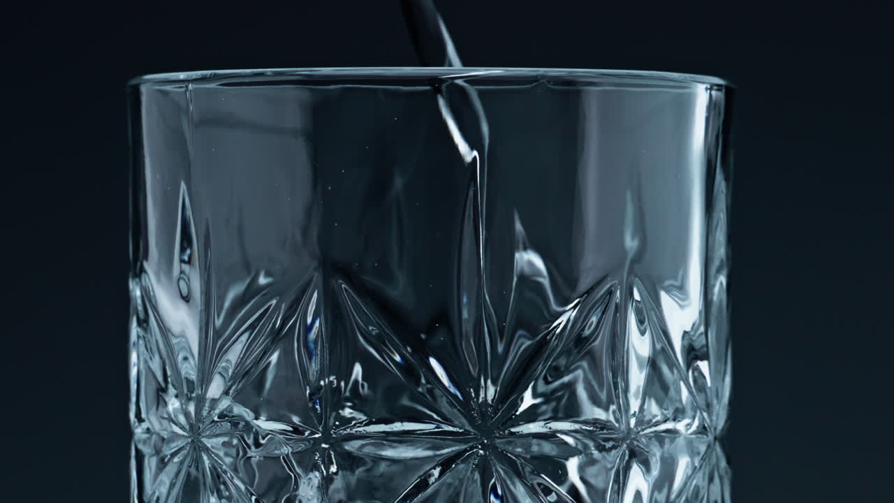 Closeup water pouring glass with splashing dark background. Crystal fresh liquid