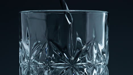 closeup water pouring glass with splashing dark background. crystal fresh liquid