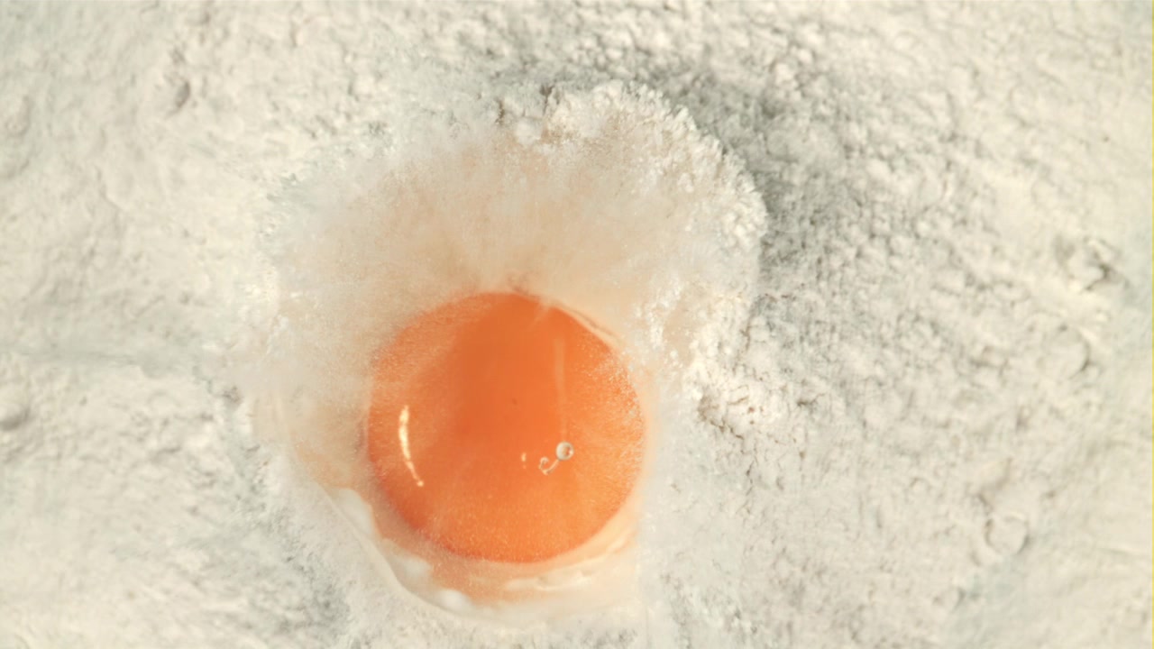 Slow Motion Egg Yolk Falling into White Flour