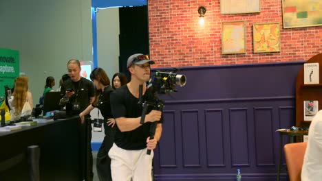 videographer shooting video with dji rs 4 pro stabilizer at ifa berlin, germany. tilt-down reveal, handheld tracking shot